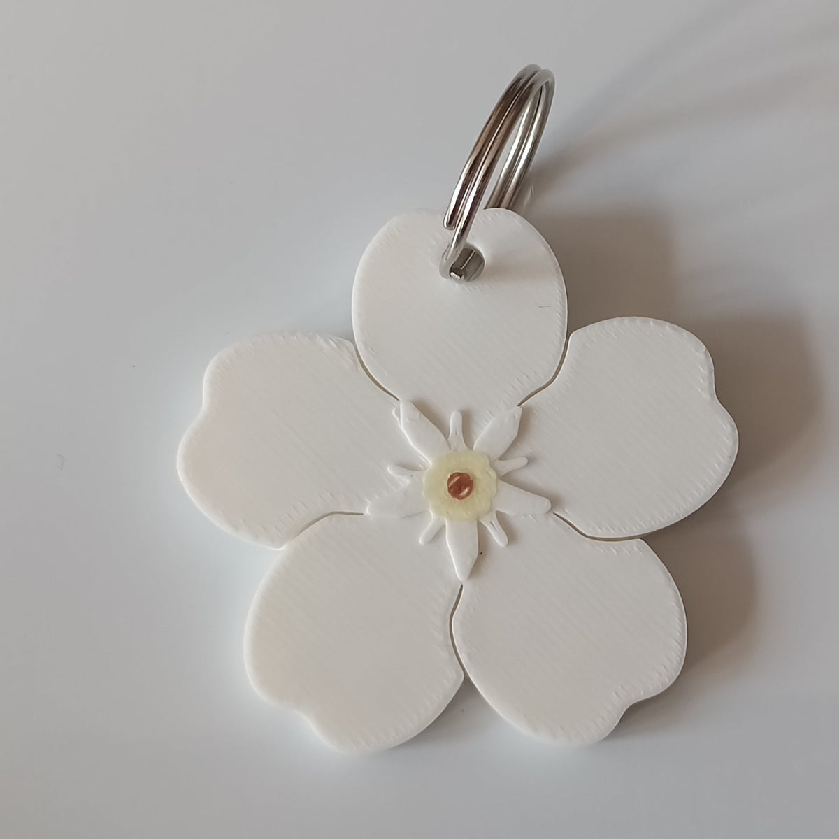 A white Forget Me Not flower pendant charm with a small silver metal ring at the top, displayed on a clean, light gray background.