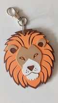 A lion head keychain charm with a metallic silver lobster clasp, featuring layered orange, brown, beige, and white details on a light gray background.